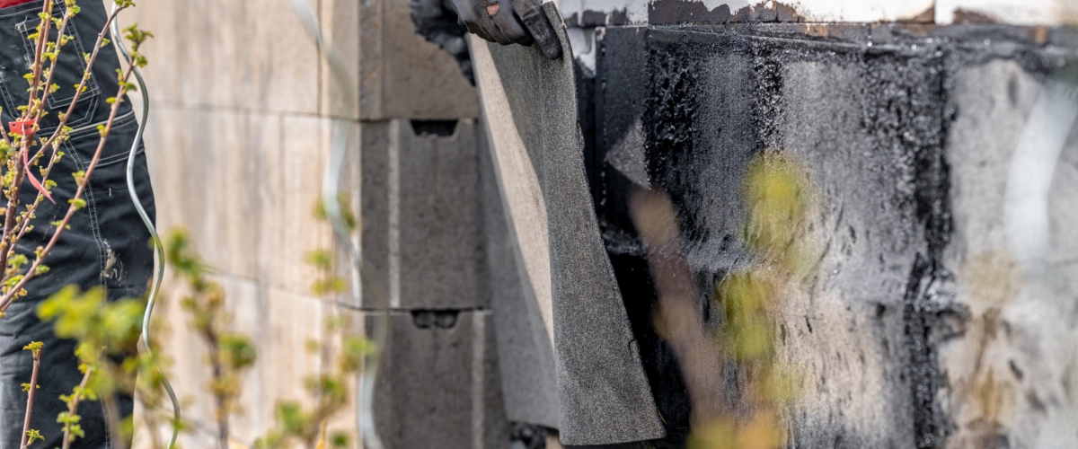 Ein Handwerker installiert eine Abdichtungsbahn an der Kellerwand, um das Gebäude dauerhaft vor Feuchtigkeit und eindringendem Wasser zu schützen.
