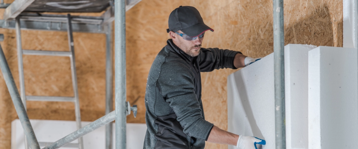 Ein Handwerker montiert große Dämmplatten an der Fassade eines Gebäudes während einer energetischen Fassadendämmung.