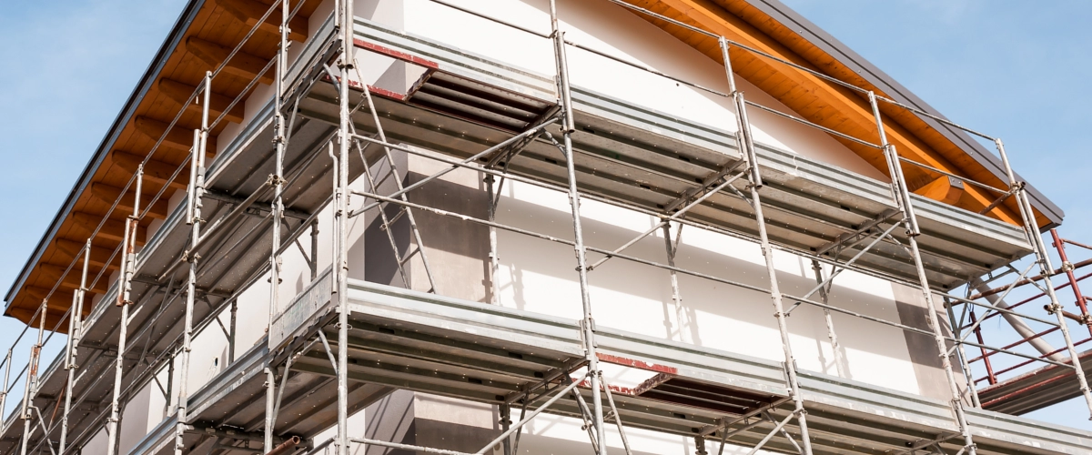 Ein Wohnhaus ist vollständig eingerüstet, während Fassadenarbeiten oder eine energetische Sanierung am Gebäude durchgeführt werden.