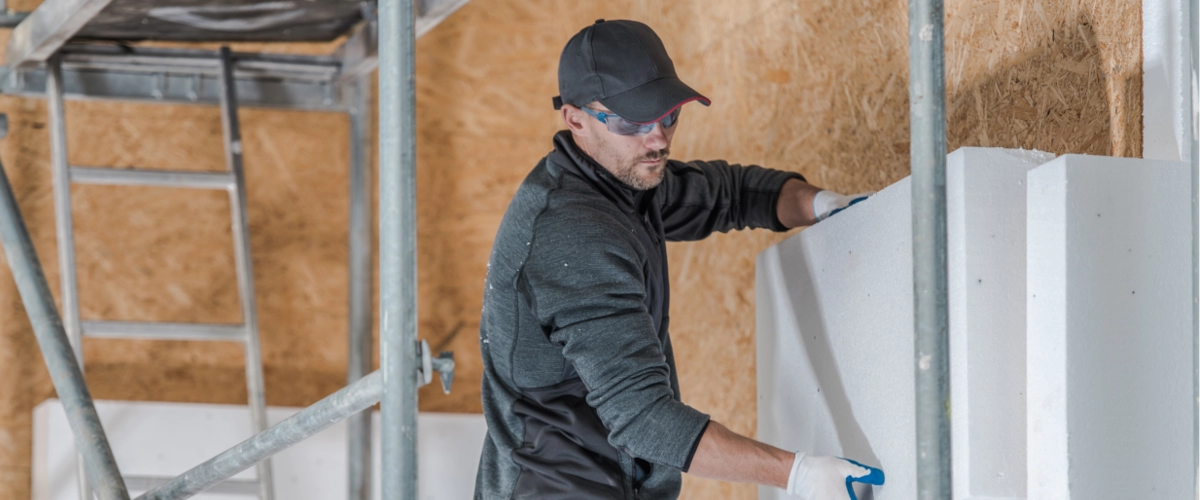 Ein Handwerker bringt große Dämmplatten an einer Hausfassade an, um die Wärmedämmung und Energieeffizienz des Gebäudes zu verbessern.