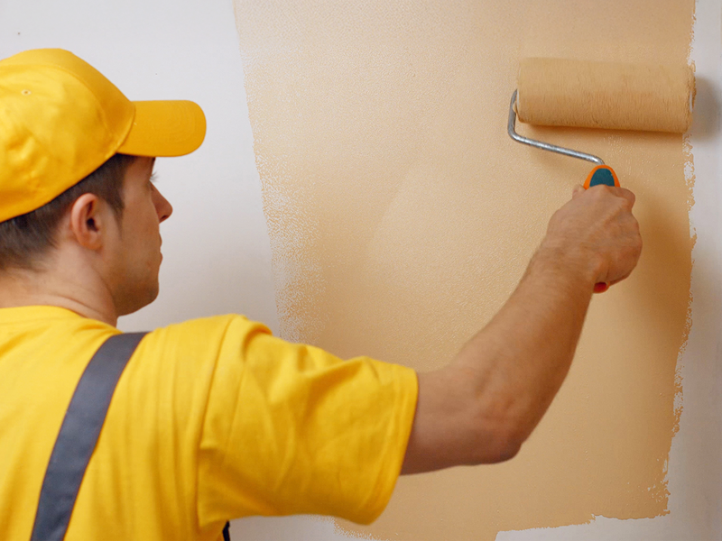 Ein Maler trägt mit einer Farbrolle frische Farbe auf eine Wand auf – typische Arbeit bei Maler- und Fassadenarbeiten im Rahmen von Renovierungen.