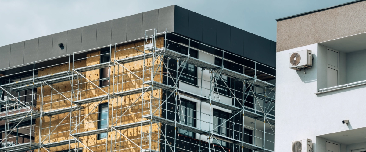 Ein mehrstöckiges Wohngebäude wird mit Baugerüst eingerüstet und erhält eine neue Fassadendämmung im Rahmen einer energetischen Sanierung.